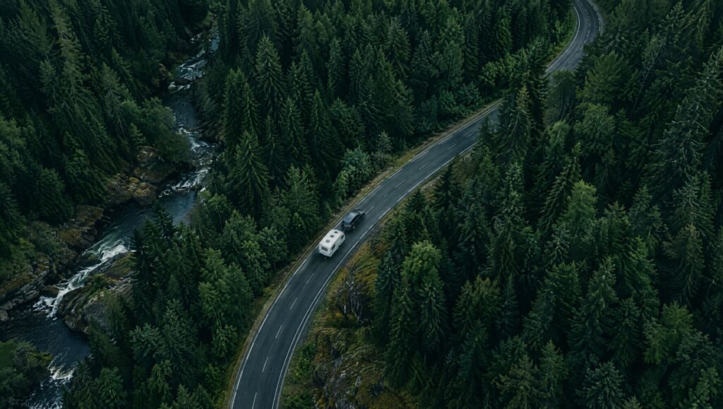 Auto mit Wohnwagen auf einer Waldstraße von oben